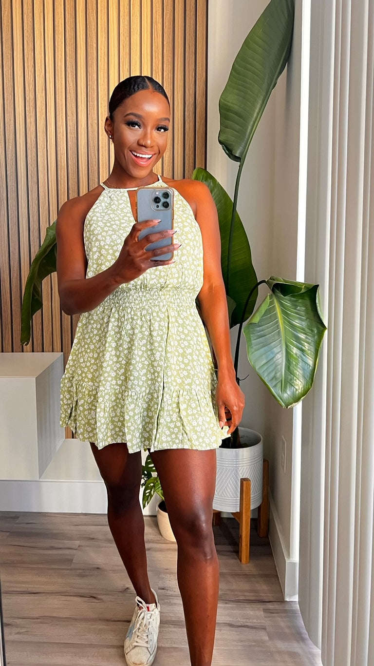 This photo shows a green romper with white floral prints. The romper has a ruffled waist and is made from 100% rayon. It is perfect for a summer day or a night out.