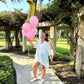 A woman with pink balloons and an embroidery white shirt and golden goose sneakers.