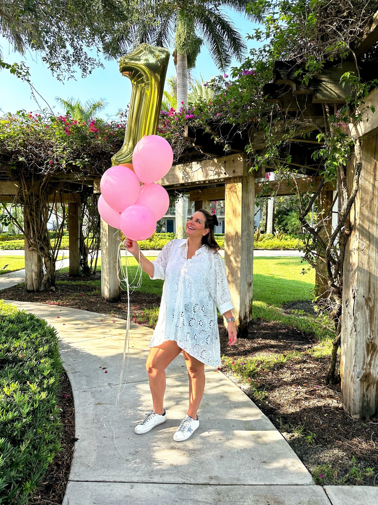 A woman with pink balloons and an embroidery white shirt and golden goose sneakers.